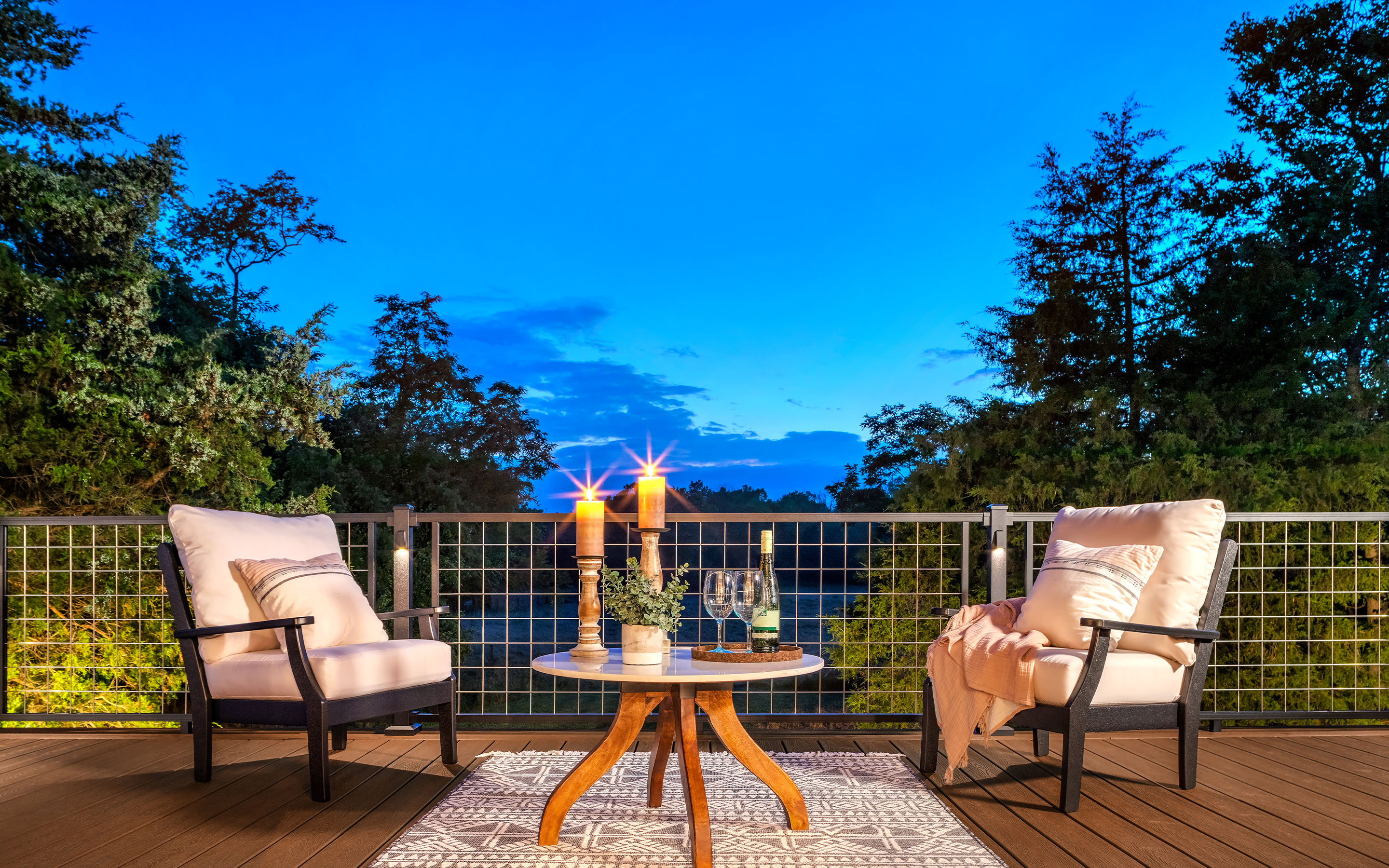 Evening Trex deck setup with modern lounge chairs, grid railing, and candlelit table — outdoor living design inspiration.